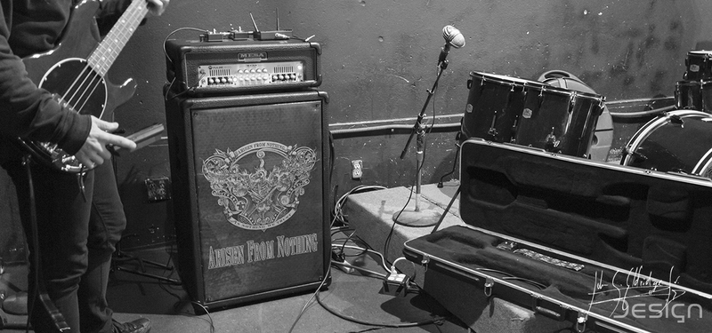 Load-in at Hailey's. Amp cabinet, staged kit, open cases. The engraved crest on the cabinet is the band's artwork, not mine.