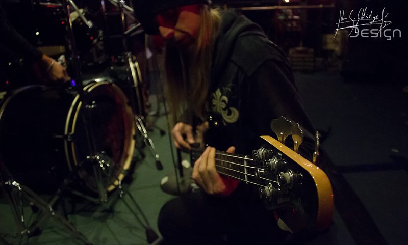 The bass player restringing side-stage while the kit gets set behind him.