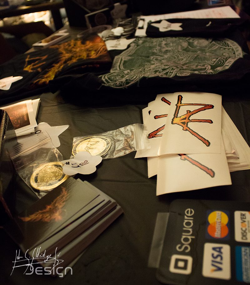The merch table before doors — CDs, shirts, stickers, challenge coins and a card reader. The night the record went out.