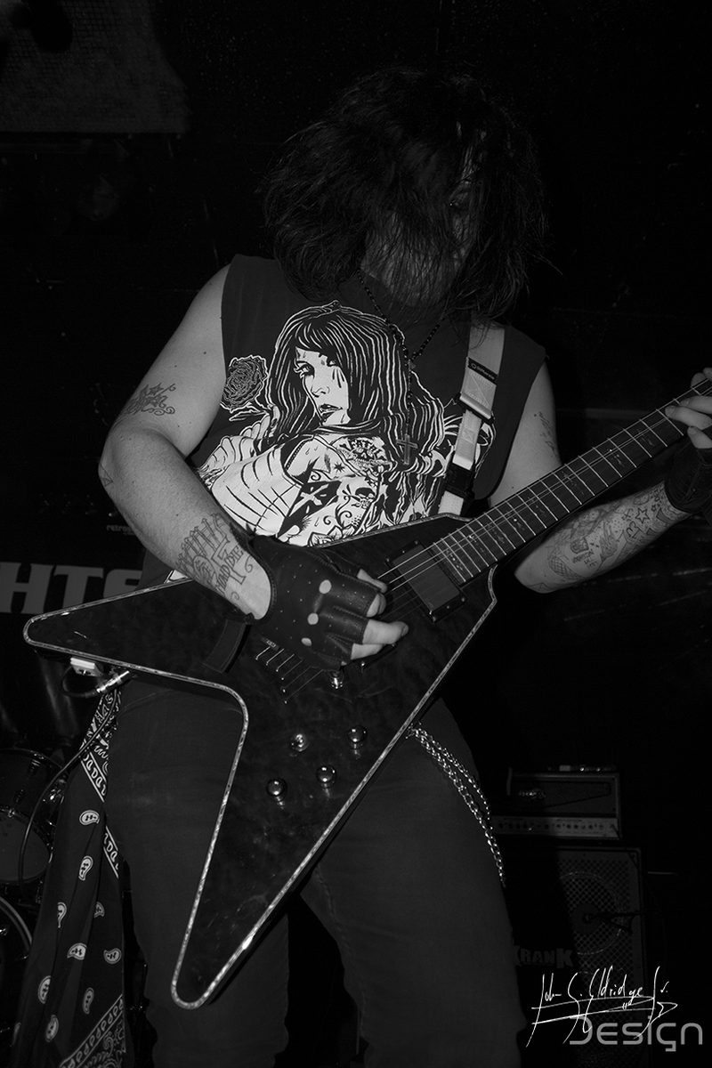 Guitarist mid-set in black and white, the venue's clutter falling away behind him.