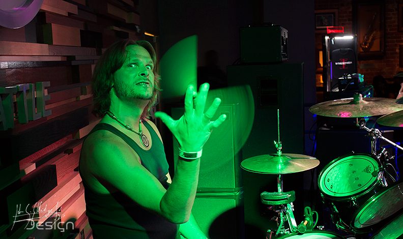 Vocalist washed in green from the house rig, kit visible behind him.