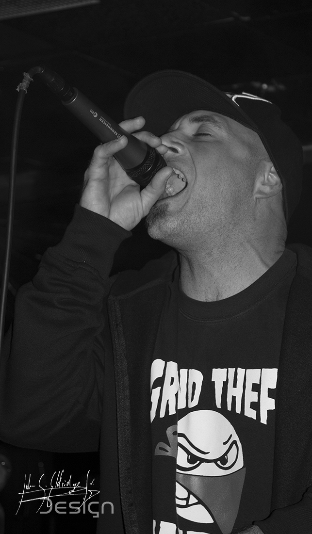 Vocalist mid-phrase, tight and high-contrast, the room behind him thrown away to black.