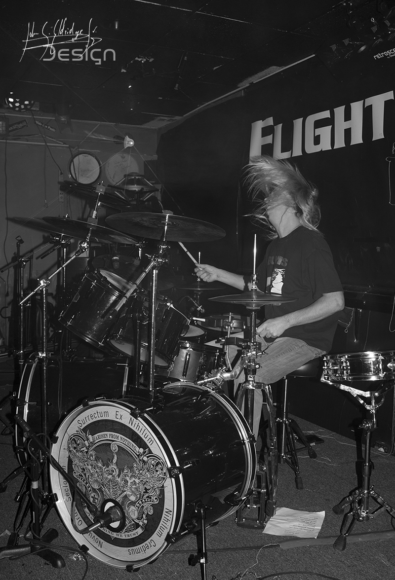 Drummer mid-set at Flight's, shot past the kit with the venue's own drum-riser sign in frame.