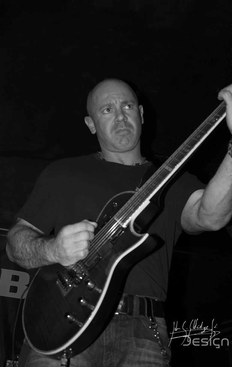 Guitarist in profile against a dark wall — one of the quieter frames in the set.