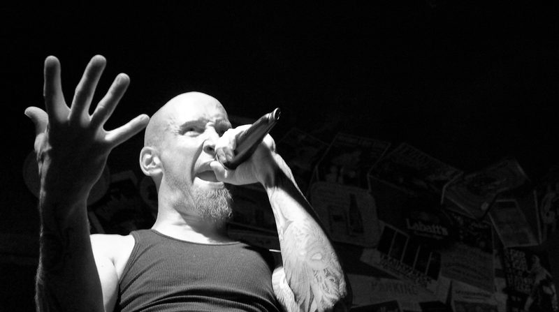 Not a studio frame — the vocalist live and low-angle, against a bar wall papered in beer signage. It ended up in the promo selects because it out-performed the posed work.