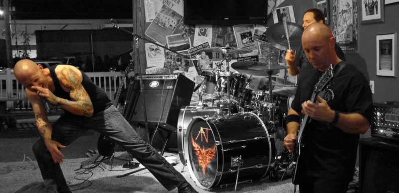 Live, treated with selective colour so the tattoos and the flame graphic on the bass drum carry while the room drops back to grey.
