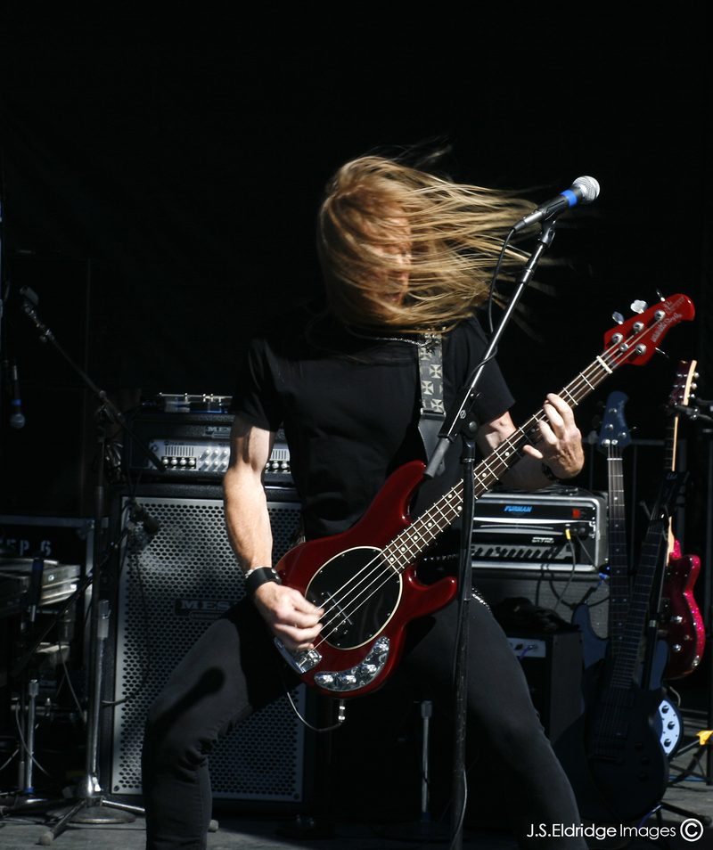 Bassist mid-set in full outdoor daylight — no house rig to work with, just sun.